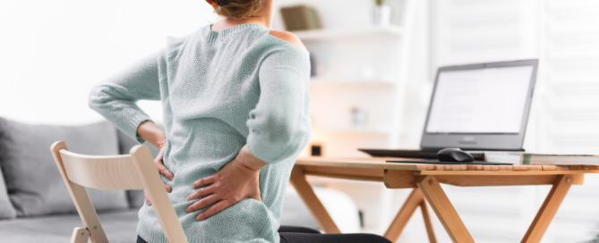 person at desk with laptop hoding lower back and hip in pain