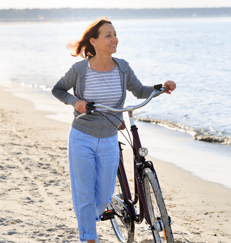 Woman on beach walking with bike