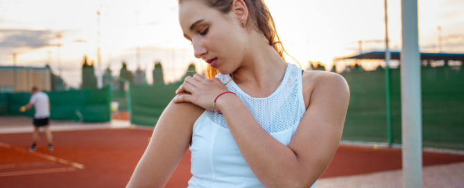 woman examining her shoulder at tennis court