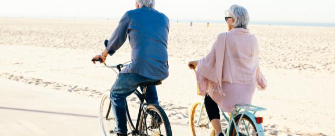 Sernior couple riding bikes along the side of the beach