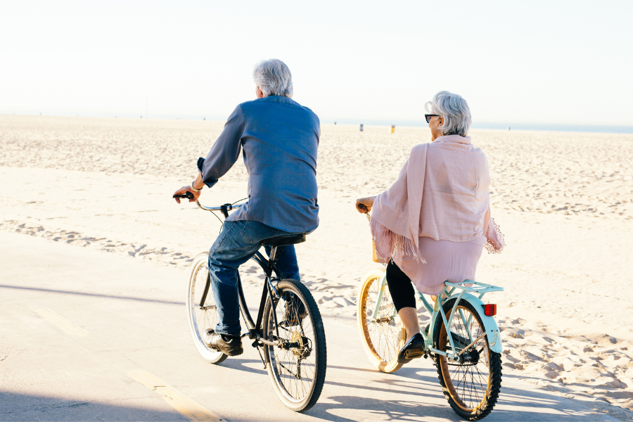 Sernior couple riding bikes along the side of the beach