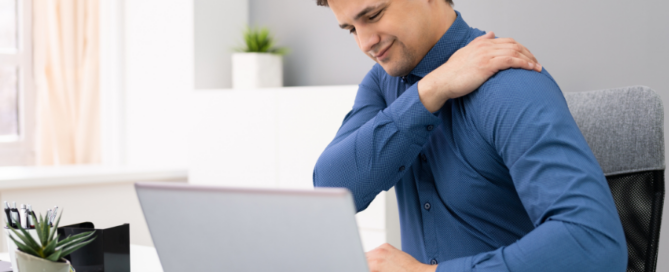 person at computer desk holding shoulder in pain