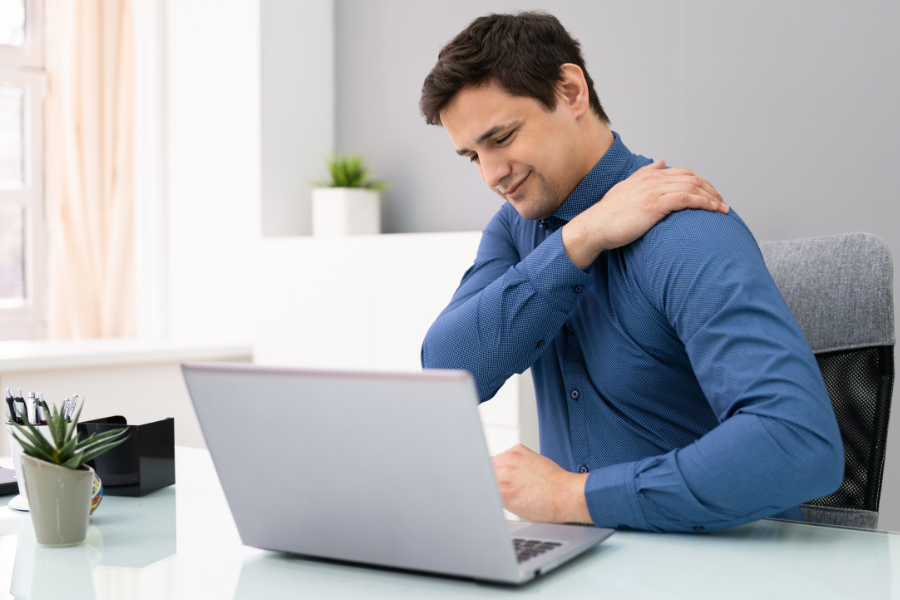 person at computer desk holding shoulder in pain