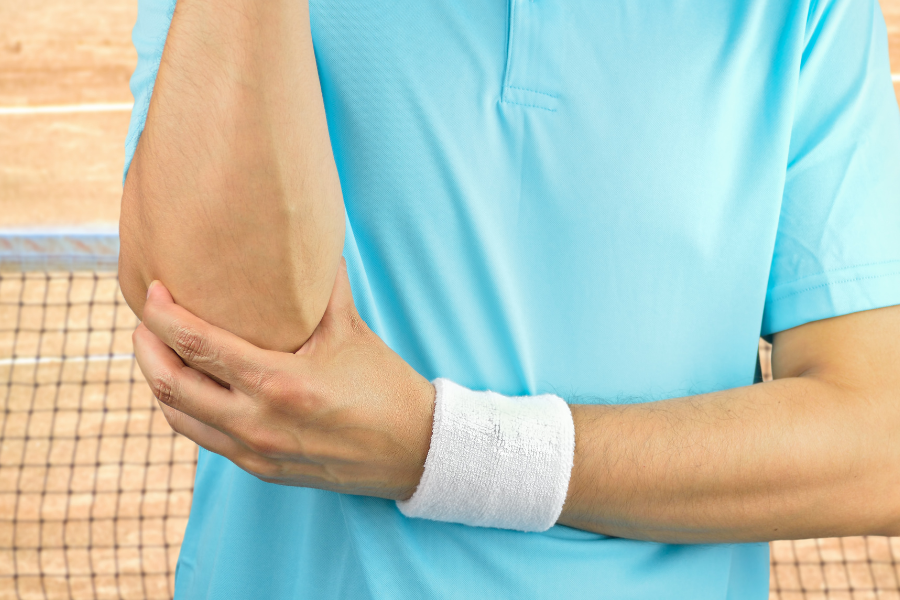 man on tennis court holding elbow in pain