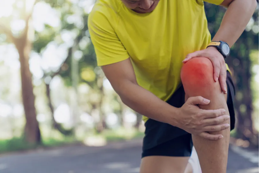 Man holding red, inflamed knee from arthritis pain outdoors
